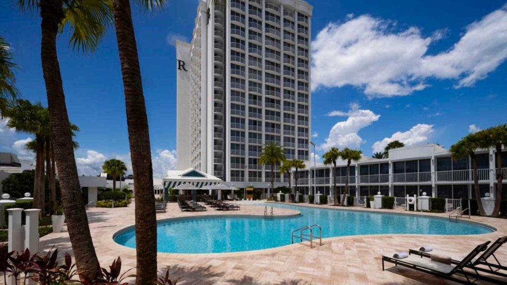 Gran hotel de lujo en Orlando con piscina circular rodeada de palmeras bajo un cielo despejado.