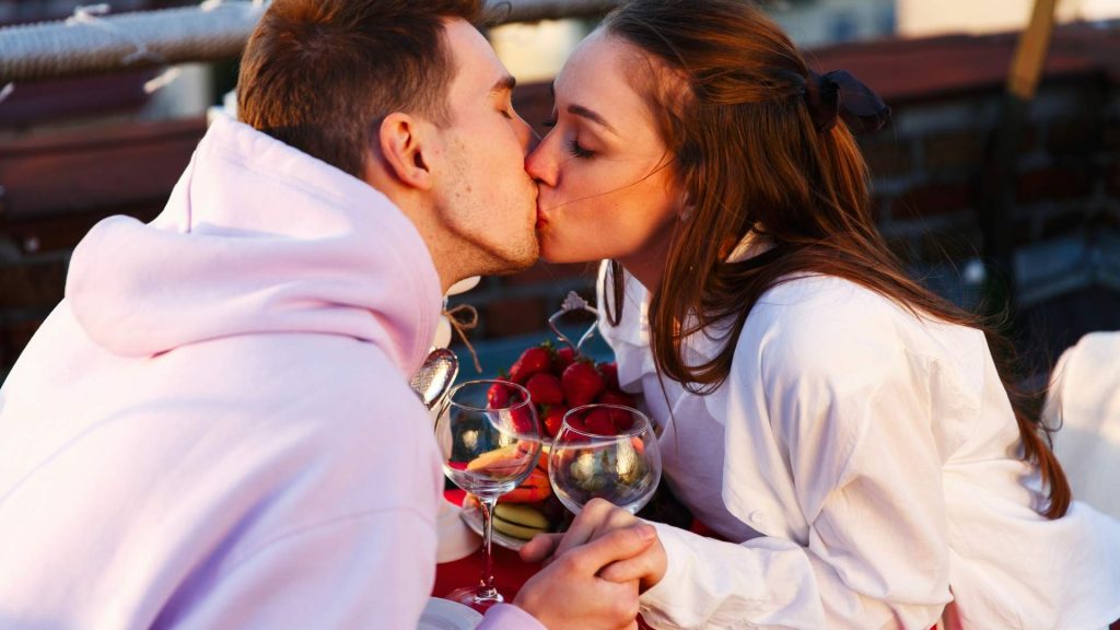 Pareja dándose un beso durante una cena privada con vino y fresas.