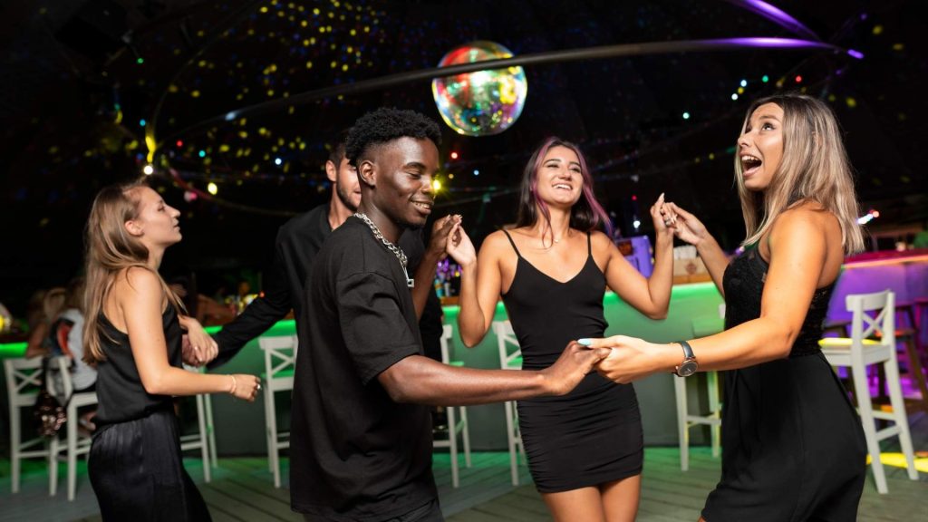 Grupo de amigos jóvenes bailando y divirtiéndose en una discoteca con luces de colores en Orlando.