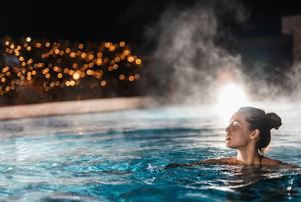 Woman relaxing in a heated pool with steam rising at night in Orlando.